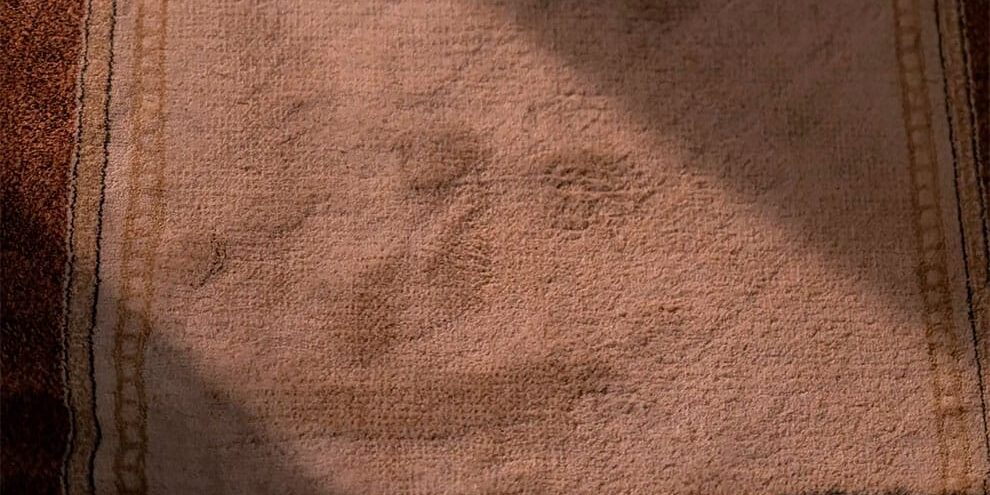 Krem-bej pamuklu banyo paspasının kahverengi kenar bordürleriyle dokulu yüzeyi, doğal ışıkta textil çekimi.