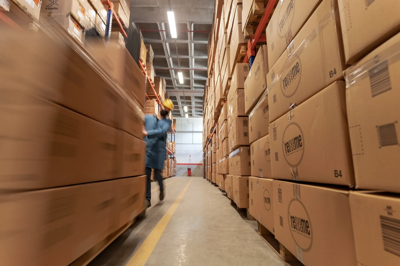 An industrial photograph showing an employee operating a forklift in a large warehouse and the logistics operations taking place there