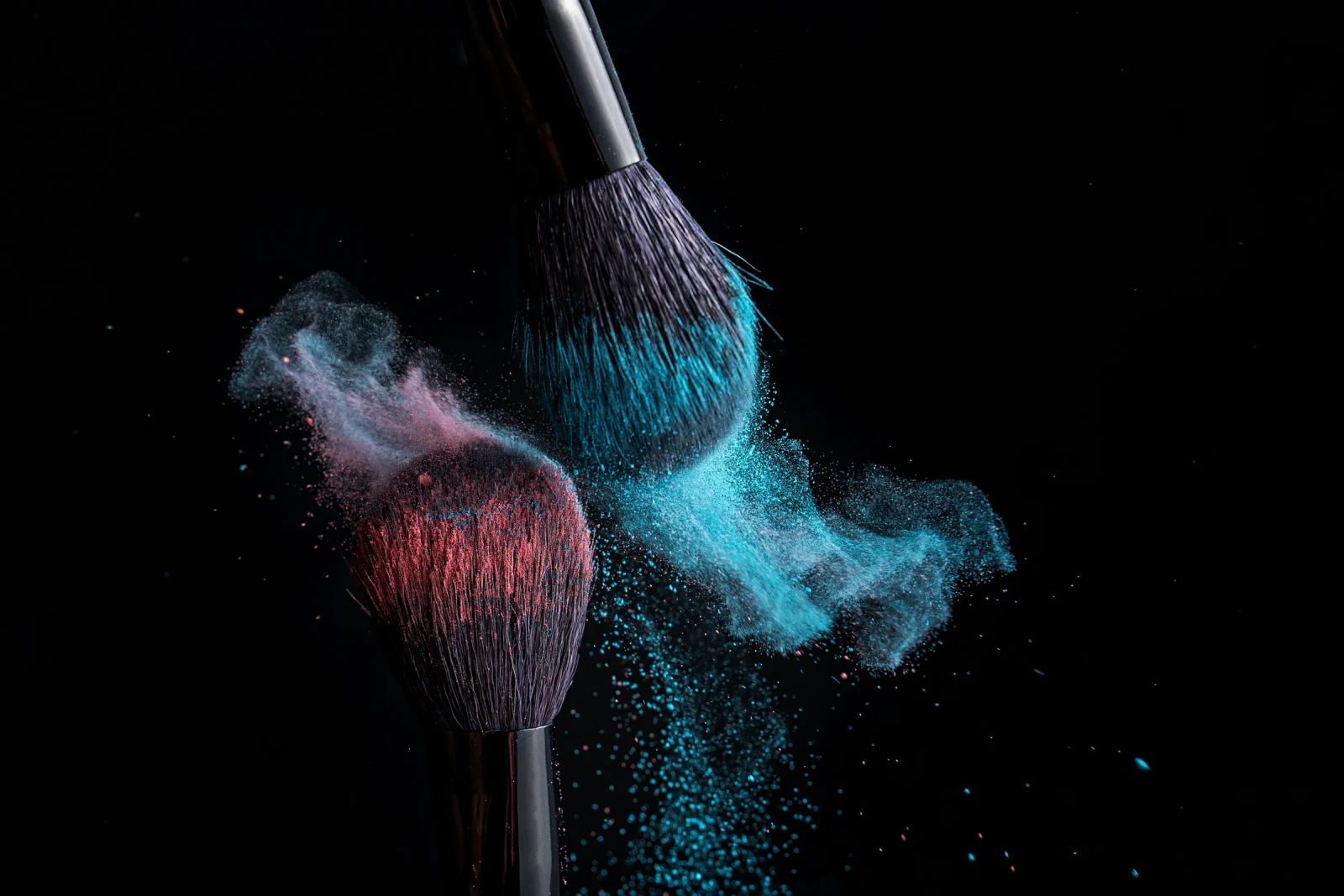 Siyah fonda iki makyaj fırçasından savrulan mavi ve kırmızı pigment tozu, dekorlu kozmetik çekimi