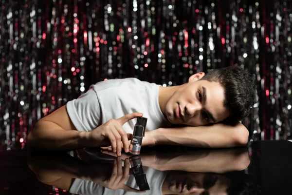 Simli siyah fon önünde siyah yansıtıcı zemine yaslanmış genç model küçük şişeyi tutan modern kozmetik çekimi.