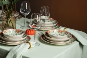 Detailverliebte Lifestyle-Aufnahme mit grün-orange marmorierten Keramiktellern, Bechern und Minikürbissen.