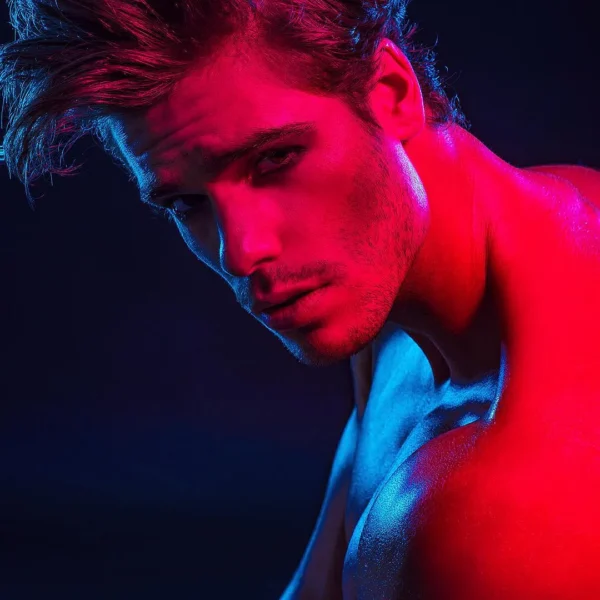 Creative editorial shot studio portrait of male face and shoulders, highlighted with red-blue neon lights.