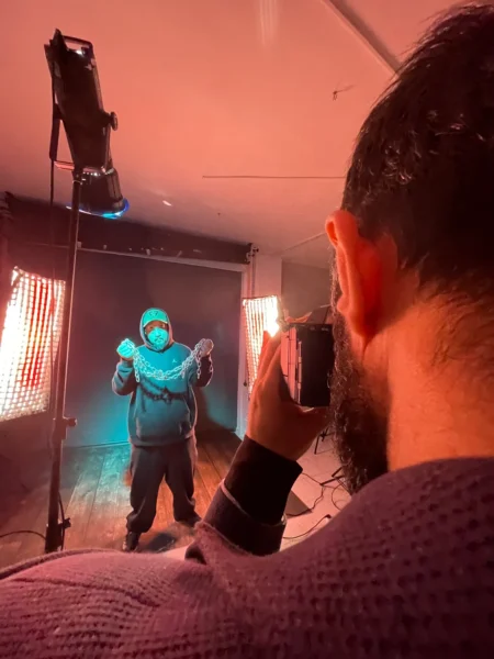 A man in a black sweatshirt holds a chain in a studio with red and blue lighting; the photographer is doing a concept studio shoot.
