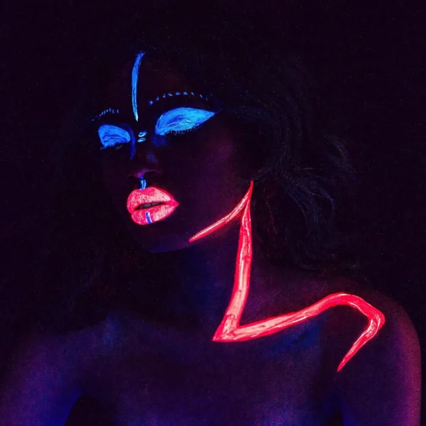 Concept portrait with blue eye makeup with UV paint and neon pink lip-shoulder line on a dark background.