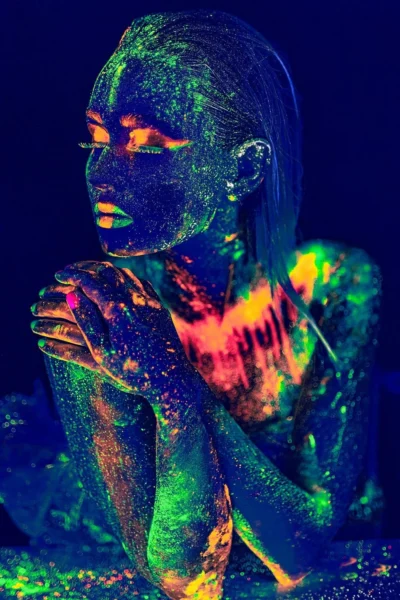 Concept portrait shot with neon UV paint with bright green-orange spots on face and body.