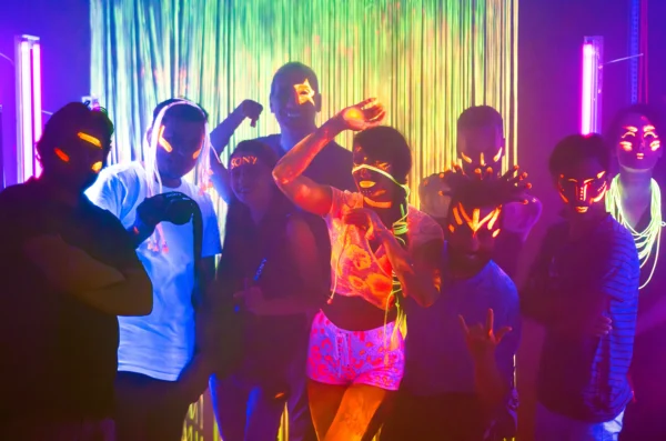 The concept of a live studio shoot with the band dancing in front of a colorful screen, their faces glowing with phosphorescent paint in neon black light.