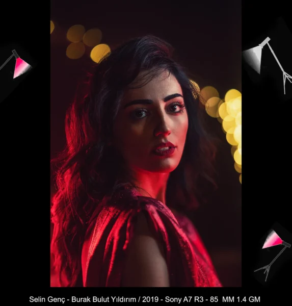 Dramatic portrait shot of woman with long wavy hair and sparkling red dress glowing in red rim light against dark background.