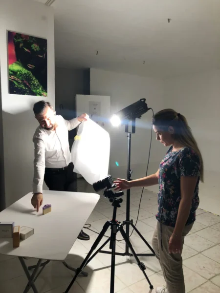 Two people placing soap boxes on a white table, detail-oriented studio shot with tripod and light, and product shot.