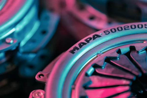 Detail-oriented macro shot of a metal clutch pressure plate labeled MAPA, illuminated in blue and pink tones.