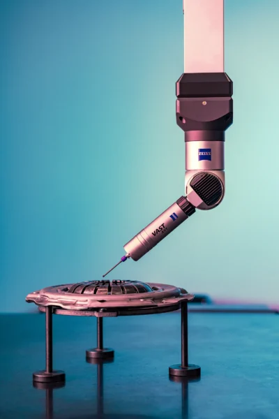 Detail-oriented industrial photography of a measuring arm touching a metal part with a fine-tipped probe against a blue-green background.