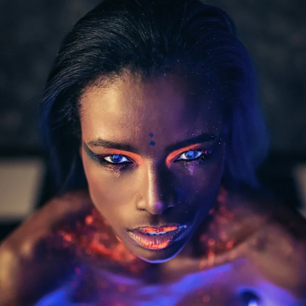 Close-up female portrait shot in dramatic light with UV orange makeup and glowing skin, creative editorial shot.