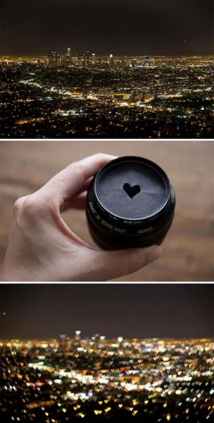 Elde tutulan lens kapağındaki yürek kesik aparattan oluşan kalp bokeh'li gece şehir manzarası, yaratıcı dış mekan çekimi.