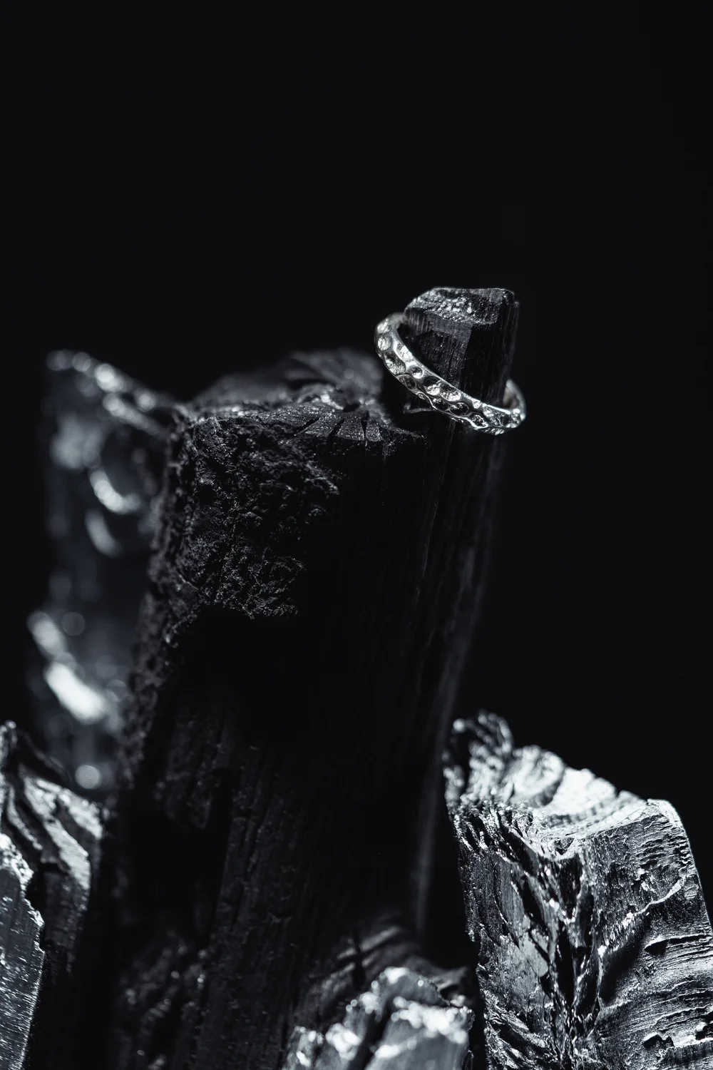 A silver ring with stone details set on pieces of coal against a dark background; a macro shot of decorative jewelry